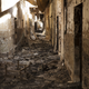 Debris litters the floor as sunlight shines through the damaged roof of a scorched corridor.